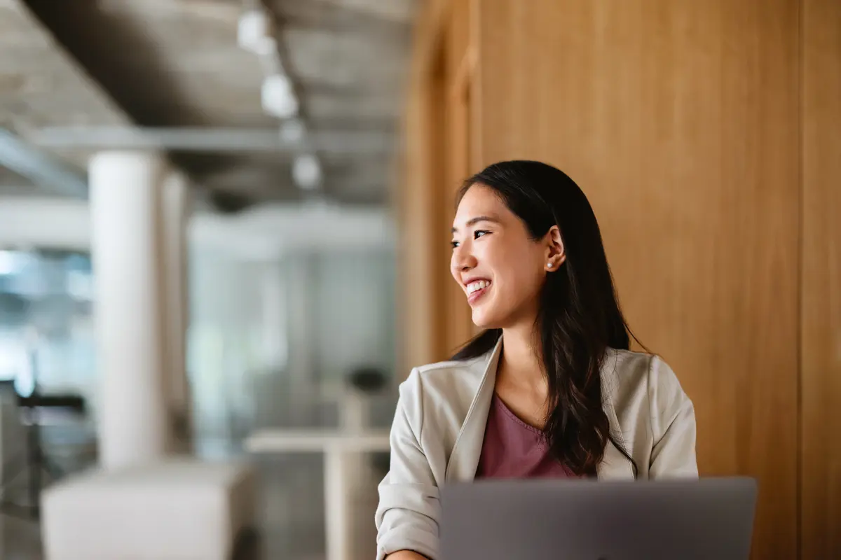 A smiling IT professional looking away from a laptop in a bright modern office