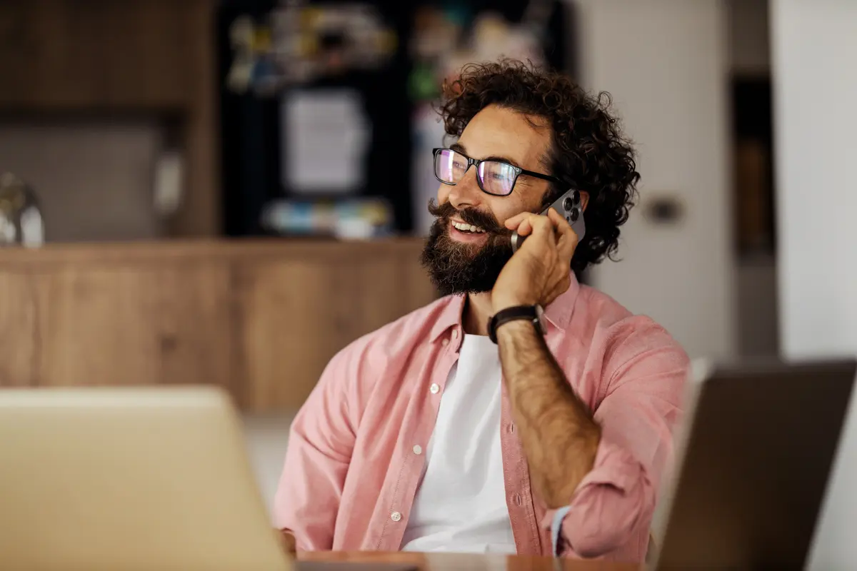 An IT professional taking a call while working at a laptop in a modern home office